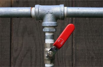 Here's an alt tag for the image: Metal pipe with red valve handle.