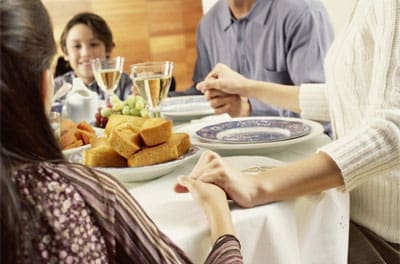 Family holding hands at dinner table.