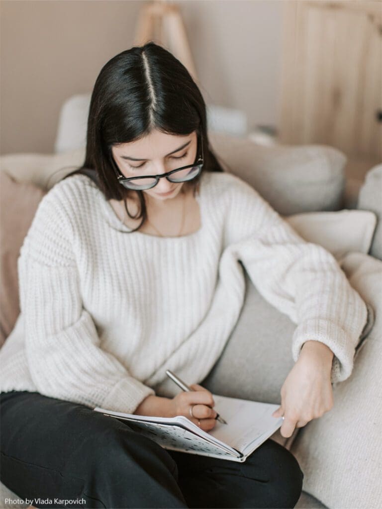 Woman writing in notebook on couch.