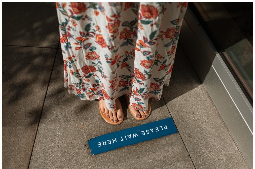 Woman's feet on "Please wait here" sign.