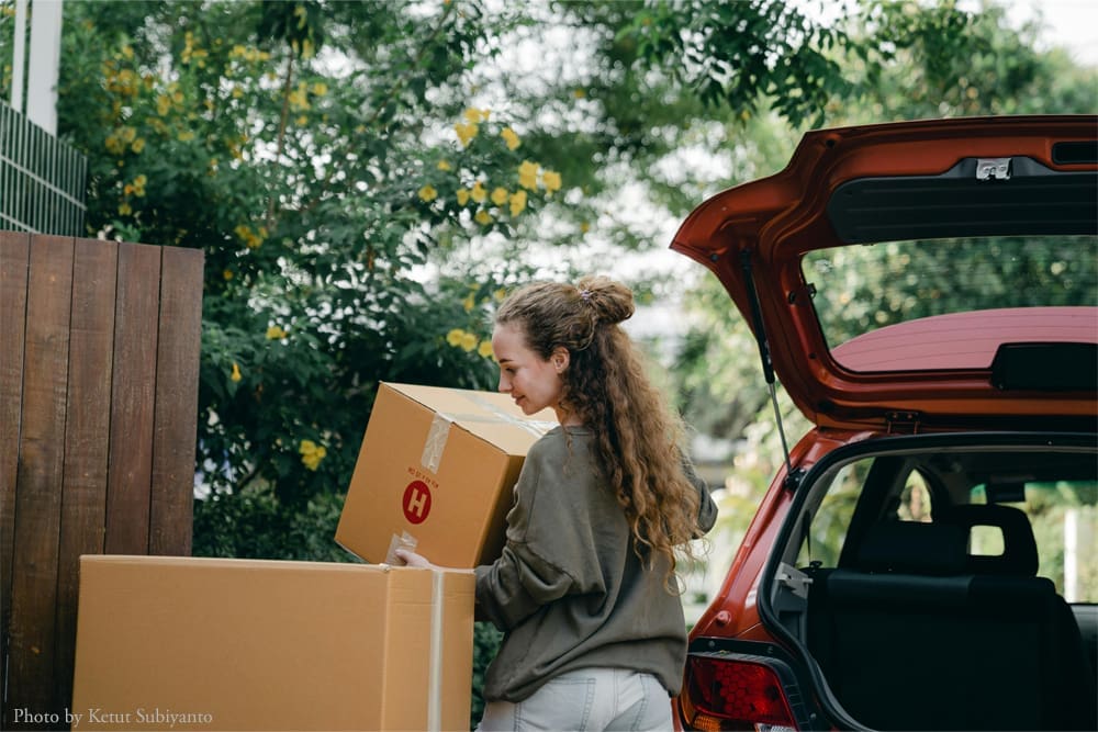 Woman loading boxes into car trunk.