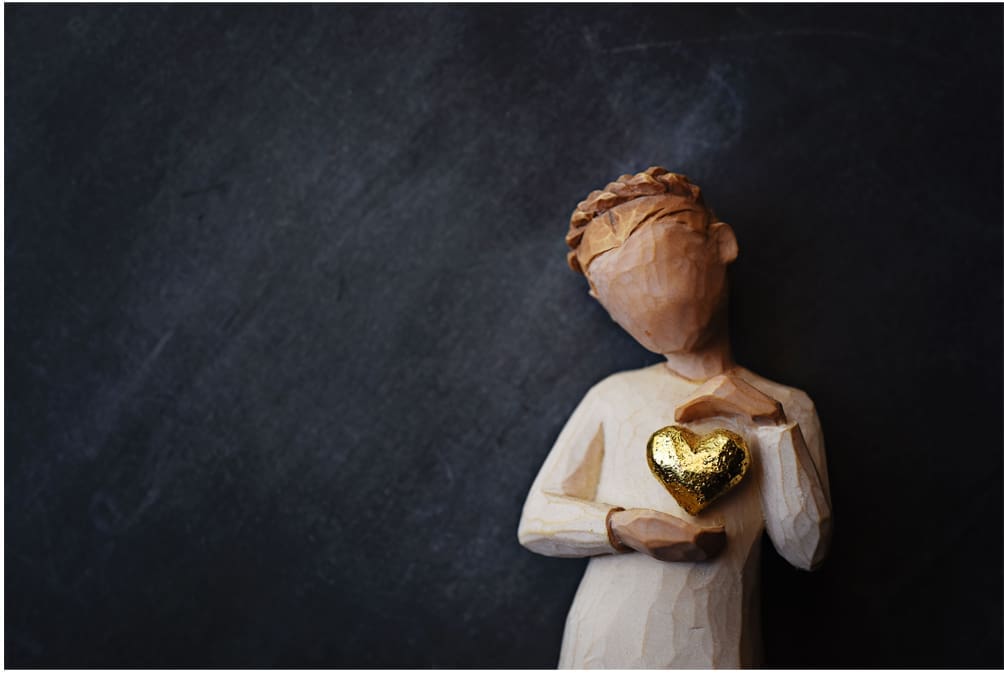 Wooden angel figurine holding gold heart.