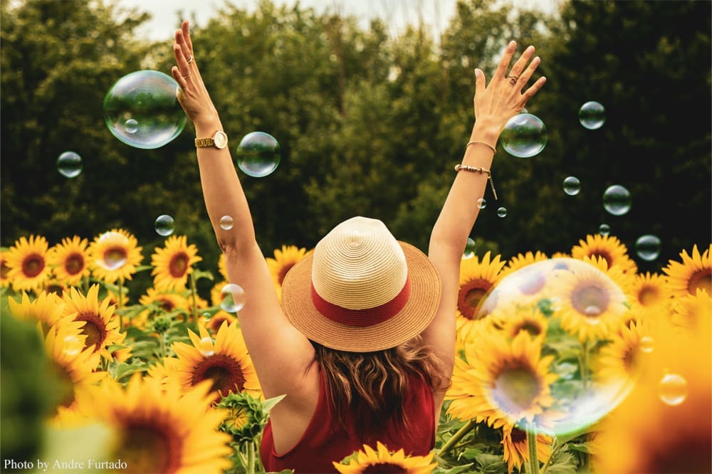 Woman celebrating in sunflower field with bubbles.