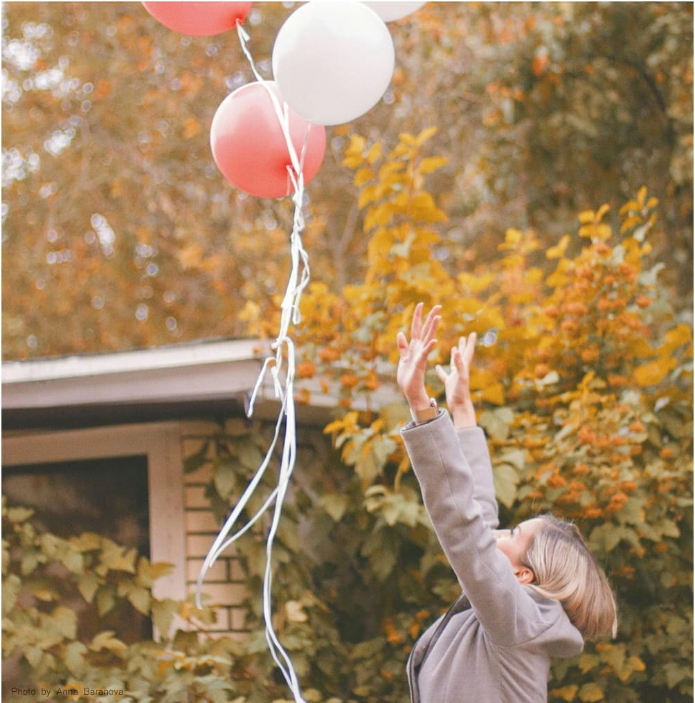 Woman reaching for balloons in autumn.