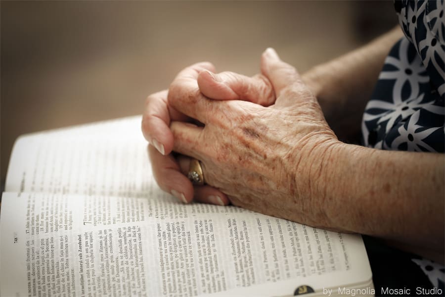 Elderly hands clasped in prayer over Bible.