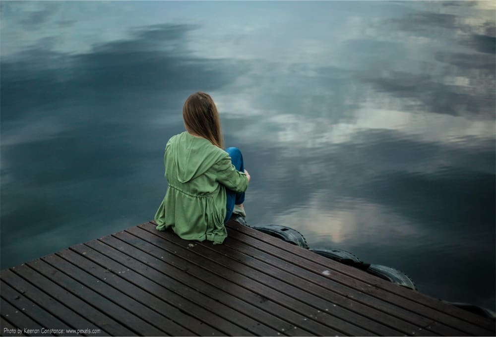 Woman sits alone by the water.