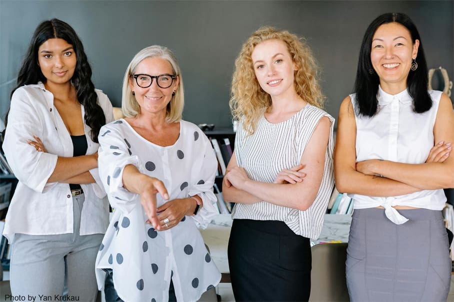 Four businesswomen stand together, welcoming.