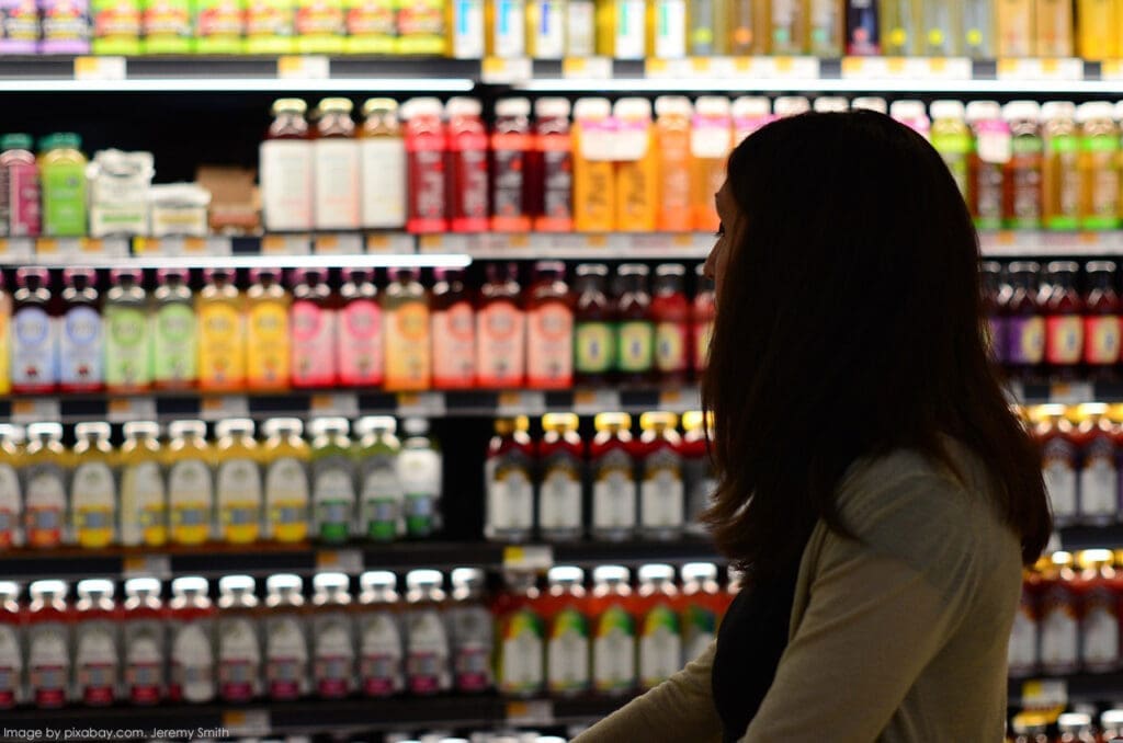 Shopper browsing colorful drinks in store aisle.