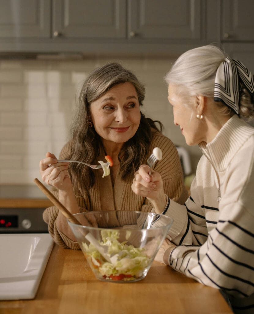 Two women enjoying salad in kitchen.