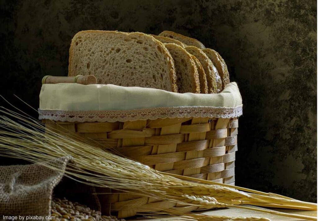 Basket with sliced bread and wheat stalks.
