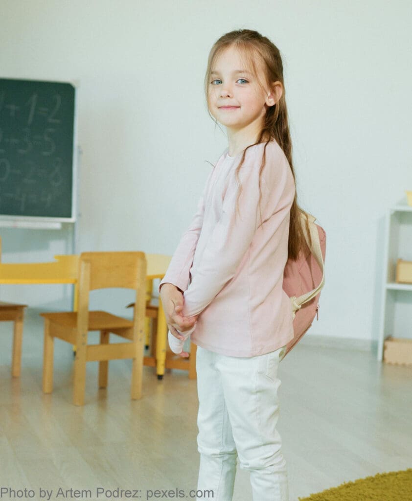 Girl smiling with backpack in classroom.
