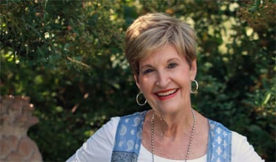 Smiling woman outdoors with greenery background.